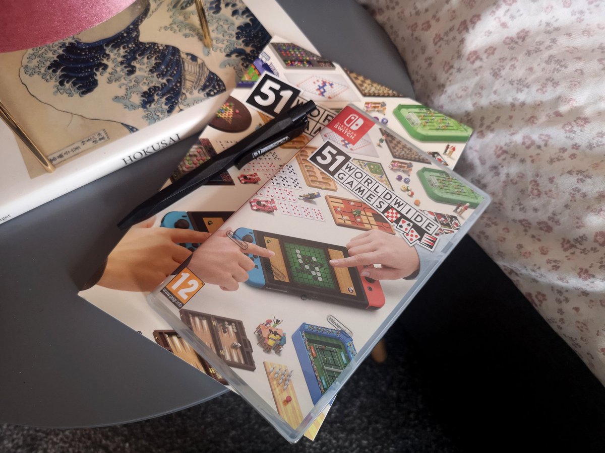 A boxed copy of 51 Worldwide Games on Nintendo Switch is on a table with a matching notebook and pen.