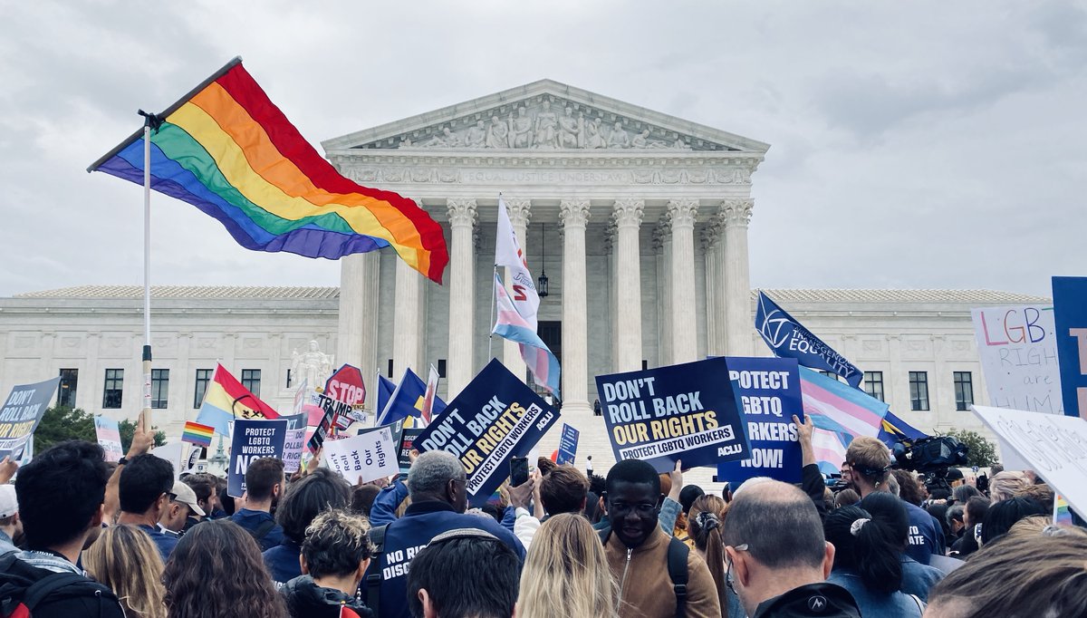 A photo from a rally outside the U.S. Supreme Court on October 8, 2019, showing pride flags and signs about protecting LGBTQ workers.
