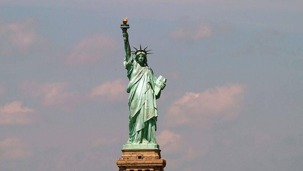 a photograph of the statue of liberty against a blue partially white cloudy sky