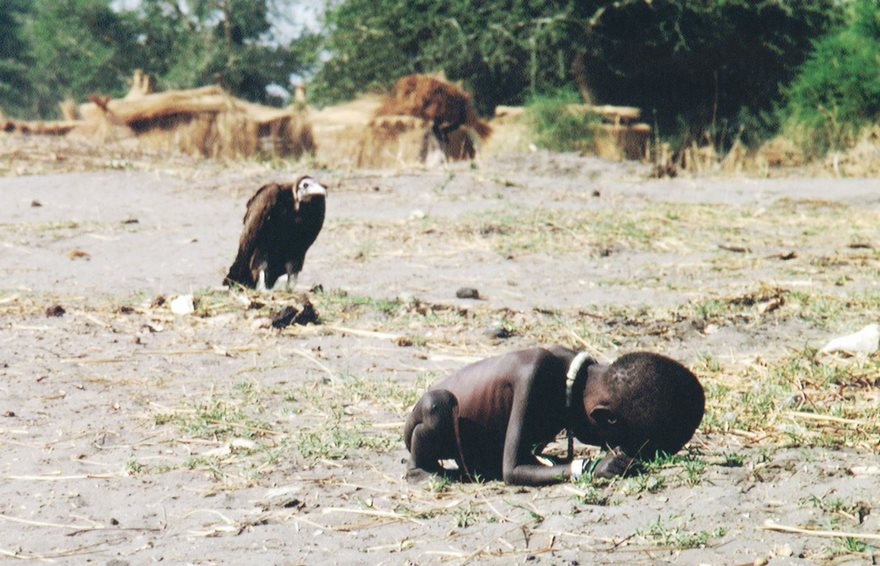 19/A famine stricken child crawling on the ground while a vulture waits in the background