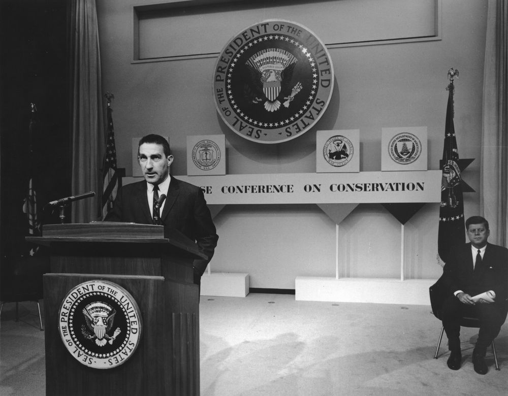 Interior Sec. Stewart Udall (foreground) speaks about conservation at event with Pres. Kennedy (background)