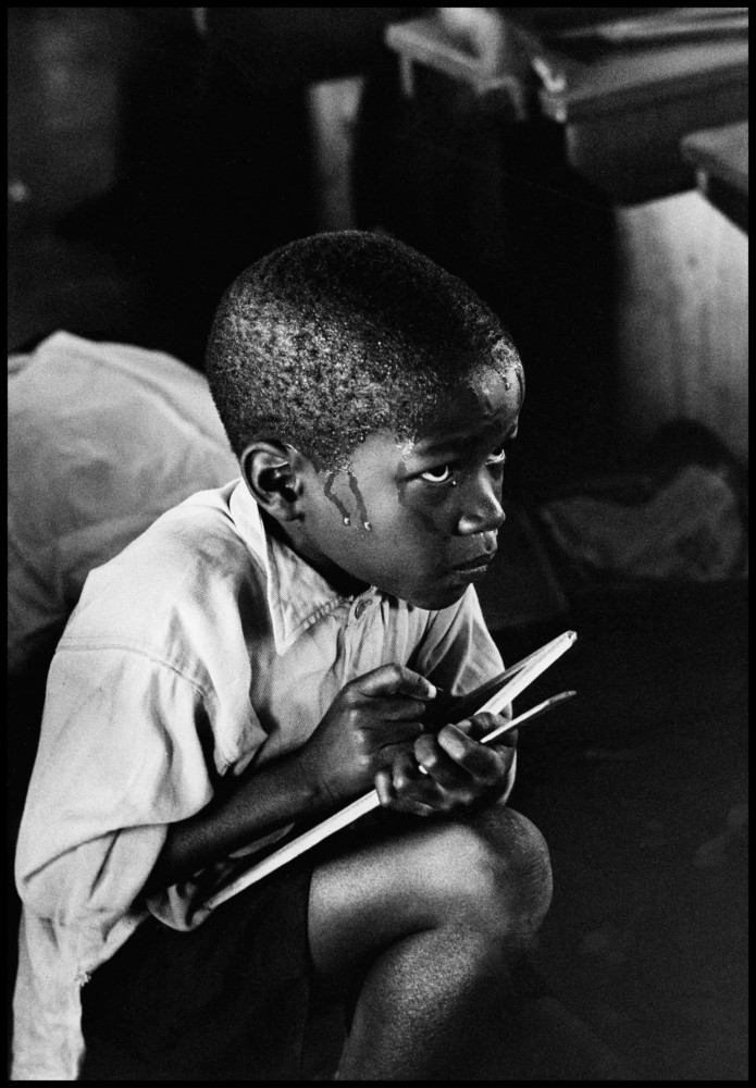 A boy squats on his haunches and strains to follow the lesson in the heat of packed classroom.© Ernest Cole