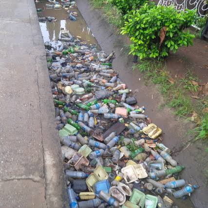 The bottle rolls and gets in a gutter alongside other non-biodegradable plastic waste.