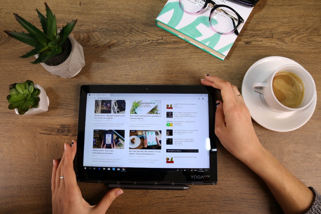 a woman sitting at a desk holding a tablet next to a succulent and cup of coffee