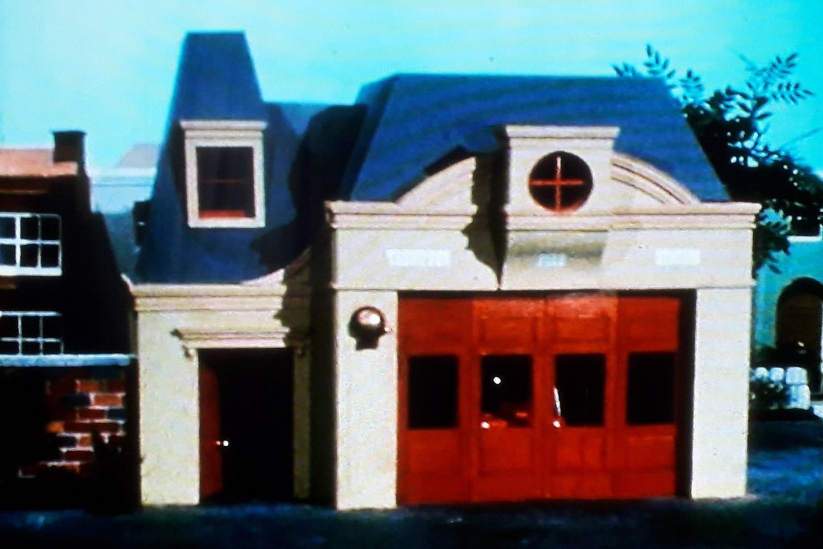 The Fire Station. Looks very, very similar to how Fire Stations really did look around then, and those big clanging doors actually looked and sounded heavy. Also note that colourful wall next to it, subtly cementing it as part of a bustling residential area.