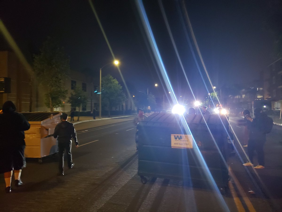 EricLicas's tweet photo. People wheeled out a pair of dumpsters and positioned them in the street, near protesters. I don't know if these are supposed to be for taking cover, but that's my plan. Protestor instructing people to get any children or vulnerable out @ocregister #SantaAna #JusticeForAndres https://t.co/HRfKyYlyGC