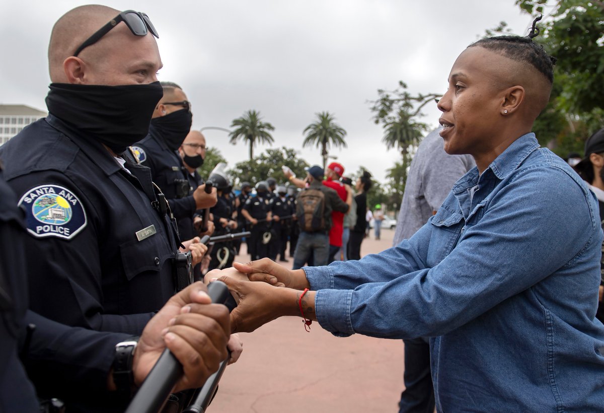 themindyschauer's tweet photo. Black Lives Matters supporter Michelle Usher holds the hand of a police officer after they fist bump during a rally. (photo by: Mindy Schauer/ SCNG)#ocprotests @ocregister #BlackLivesMatter https://t.co/DlCh3tvfpr