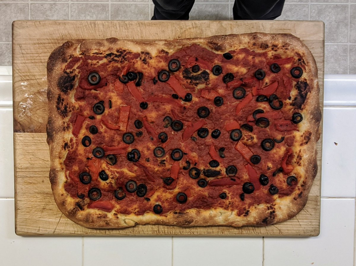 The same pizza, out of the pan and on a wooden board. The crust is cooked to a rich brown, with some darker (but not burnt) spots.
