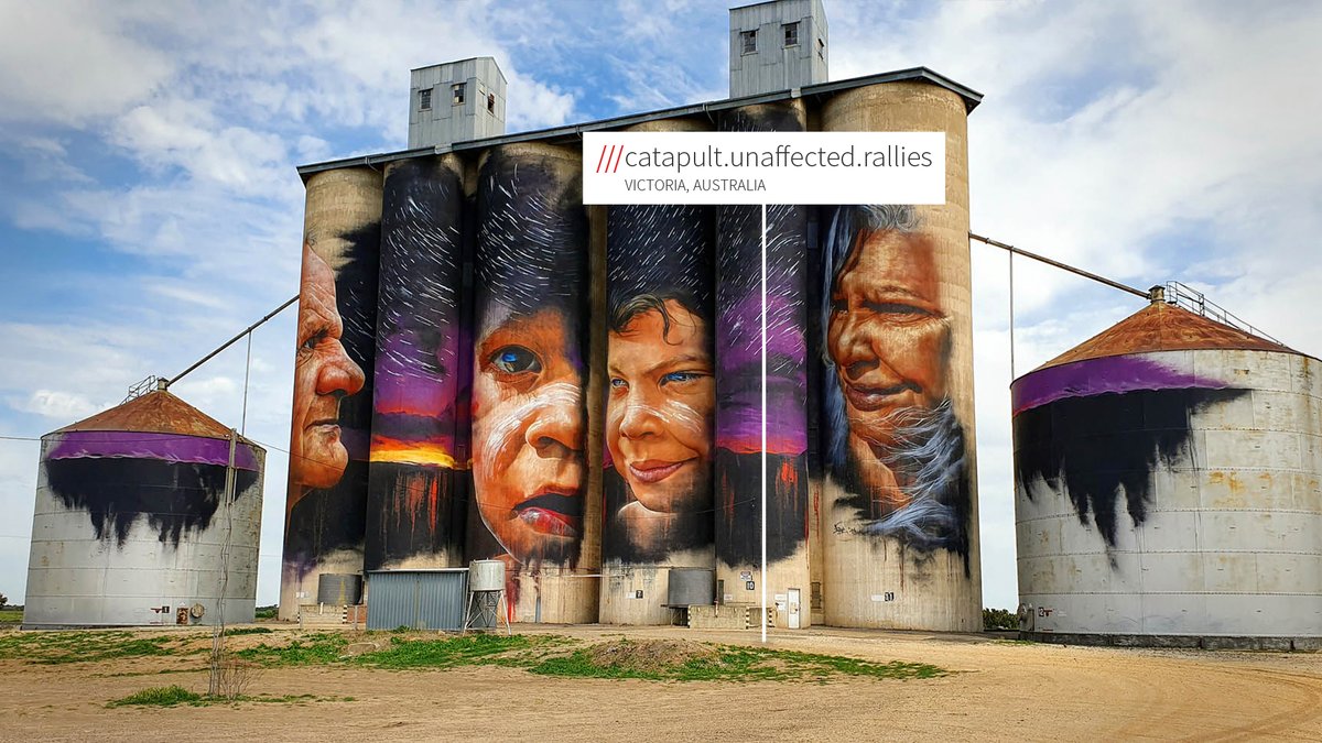 A disused silo at ///catapult.unaffected.rallies that has been painted by an artist; depicting four different faces against a dramatic sunset