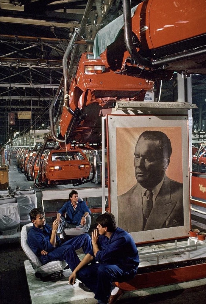 Workers in a Yugoslav car assembly plant taking a break next to a portrait of Tito. Photo by Steve Mccurry.