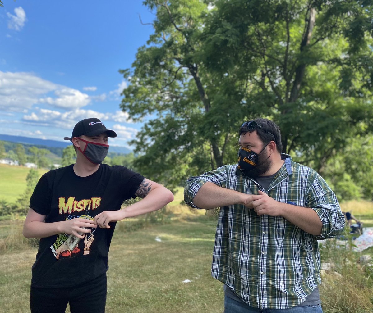 Two people bump elbows as a greeting. Both people are wearing masks. 