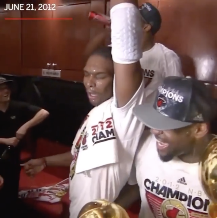 Miami Heat players, including one wearing a "2012 CHAMPIONS" shirt and another in a "CHAMPIONS" cap, celebrate in a locker room on June 21, 2012, with a championship trophy visible—capturing the moment of their hard-earned first title after years of playoff struggles.