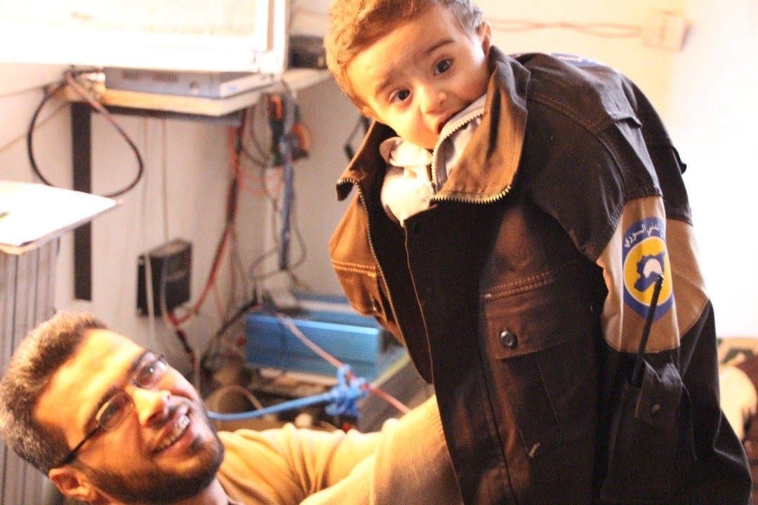 SyriaCivilDef's tweet photo. Little Mohamad doesn't know his dad's a hero or that he spends long hours every day at the service of Syrians, protecting &amp; providing for them. He only knows that it's fun to try on Dad's jacket &amp; play. White Helmet Safwat is one of our dedicated, hardworking volunteers in #Idlib https://t.co/78piKqh1sN