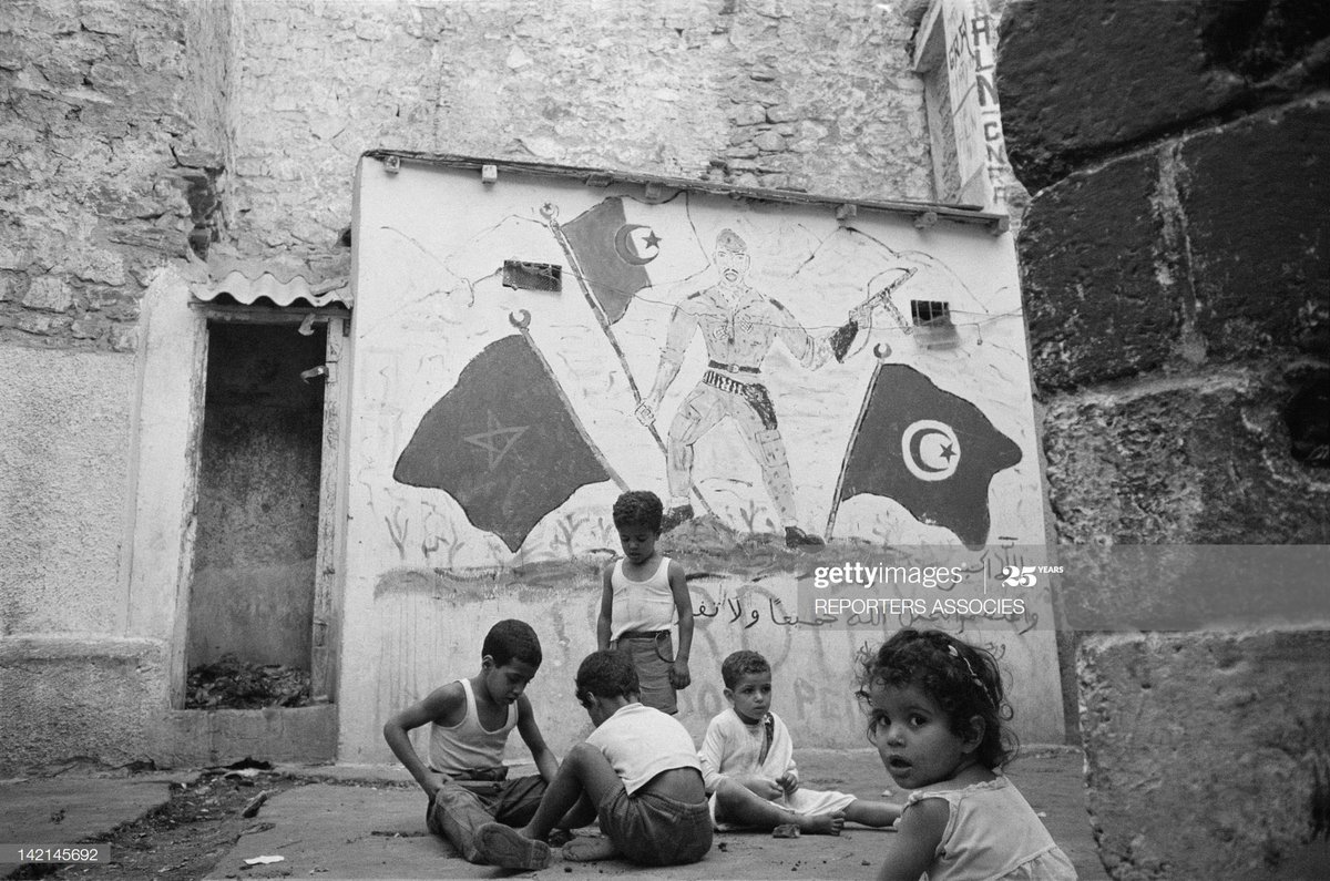 Children playing in the street during independence celebrations in Algiers, behind them flags of Algeria, Morocco, and Tunisia