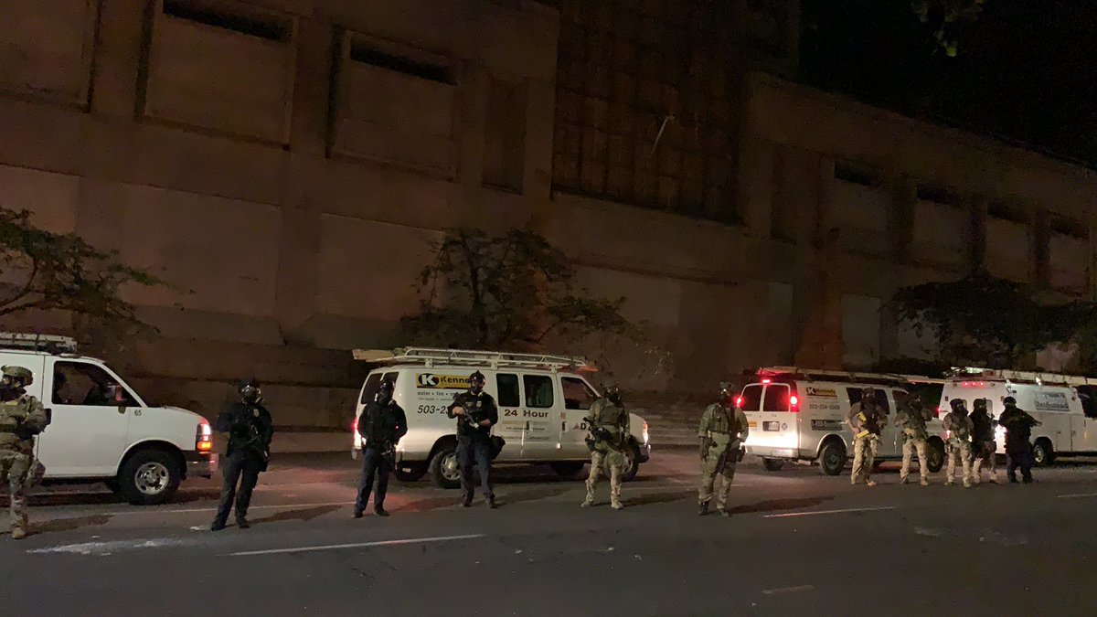 Construction vans are lined up to move out. Feds push protesters back to the sidewalk.