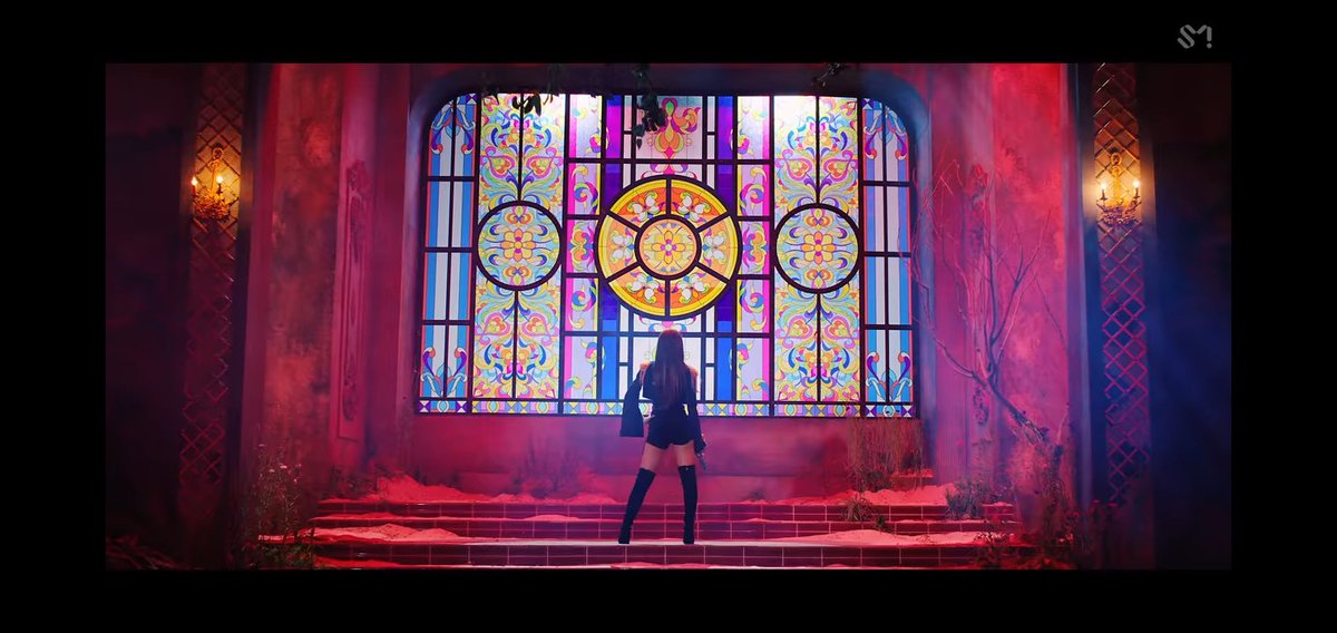 123.1. Next, you see Seulgi here. Facing again a window. (A stain glass window in specific). She's looking at the window. Meaning she's focused. Her principles in life, in how she acts and all, are seen in the colors of the glass. Yellow, Orange, Blue and Light Blue.