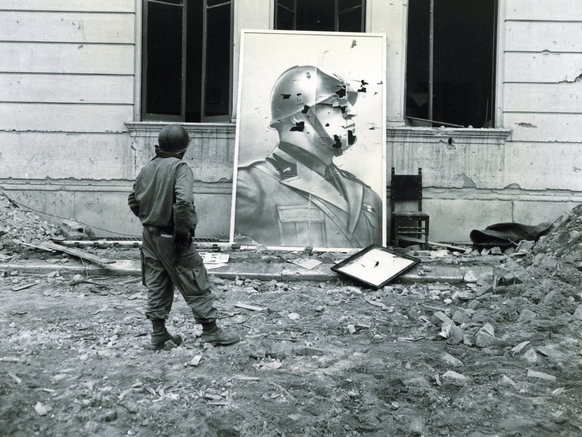 American soldier inspecting a bullet-ridden portrait of Mussolini during the Battle of Anzio, 1944.