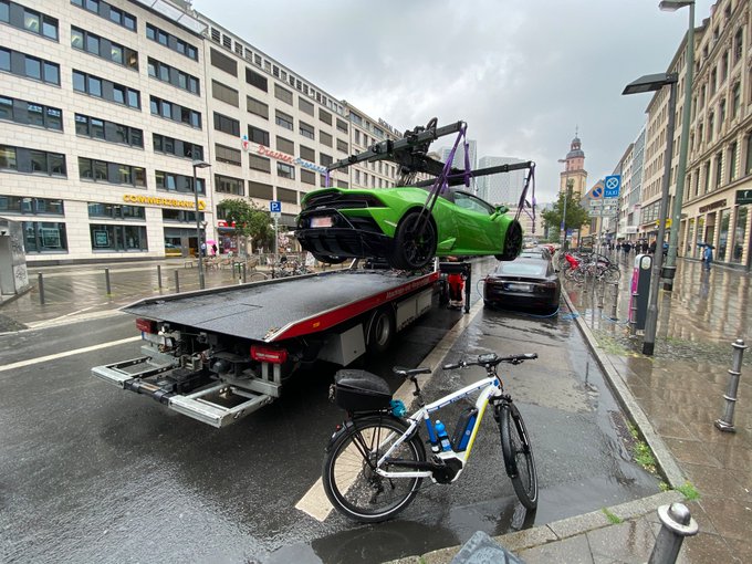 Zusehen ist ein Abschleppfahrzeug, welches gerade einen falsch geparktes Fahrzeug der Marke Lamborghini auflädt. Der Fahrer oder die Fahrerin hatte das Fahrzeug verbotenerweise an einer Ladesäule für E-Fahrzeuge abgestellt. Veranlasst wurde dies durch die Fahrradstaffel der Polizei Frankfurt. Ein Fahrrad dieser Polizeieinheit ist im Vordergrund zu sehen.