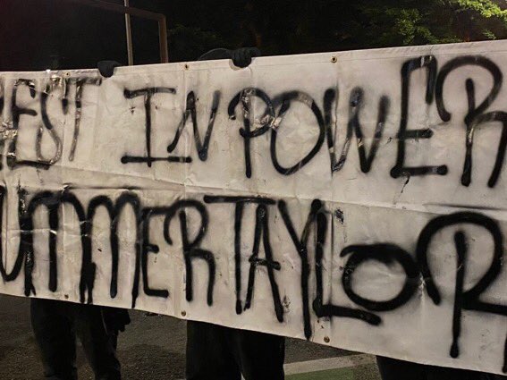 At about 10:20, folks in black with this Summer Taylor banner show up by the courthouse, and stand quietly, joining a crowd lining 3rd. Folks in street tend to be standing, folks on the courthouse sidewalk are primarily sitting. This looks like one demo at this point. 6/