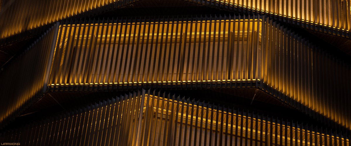 Photography by Liam Wong of Tokyo at night - focusing on simple shapes and color in architecture. This image is a yellow modern structure shapes like several octagonal coins stacked on each other.