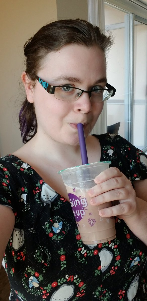 White girl in a black Totoro dress sipping a milk tea and looking into the camera.