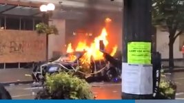 With a hard cut, the video switches to the busted out roof of a car. Protesters dance atop it. Later, it is seen on fire.