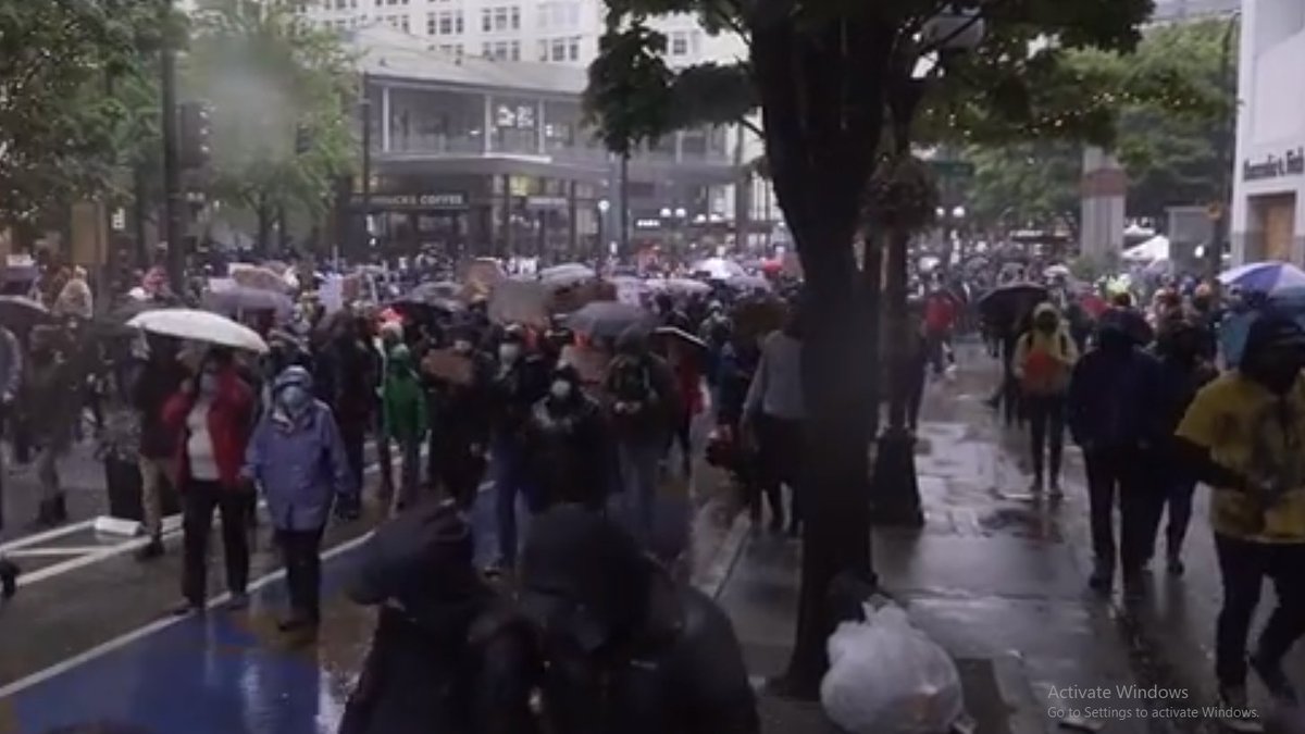 A few minutes later, the protesters have acquired many more umbrellas and use them to provide overhead cover from the continuing explosions as gas canisters land around them over the course of the day.