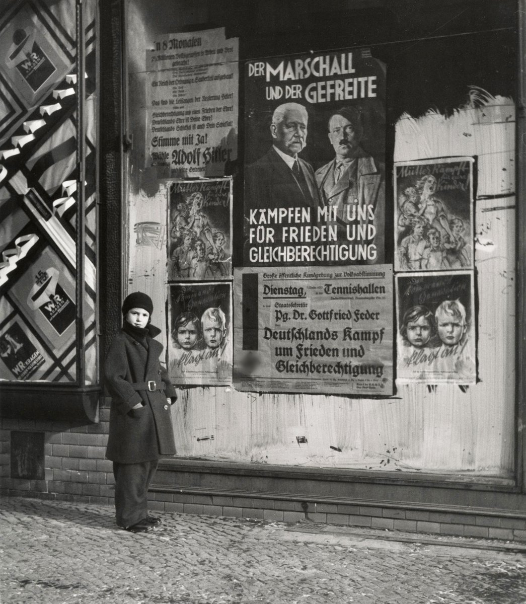 Photo taken by the photographer Roman Vishniac in Berlin, 1933, with Vishniac’s daughter posing next to election posters. The one with Hitler and Hindenburg reads: “The Marshal and the Corporal fight with us for peace and equality”.