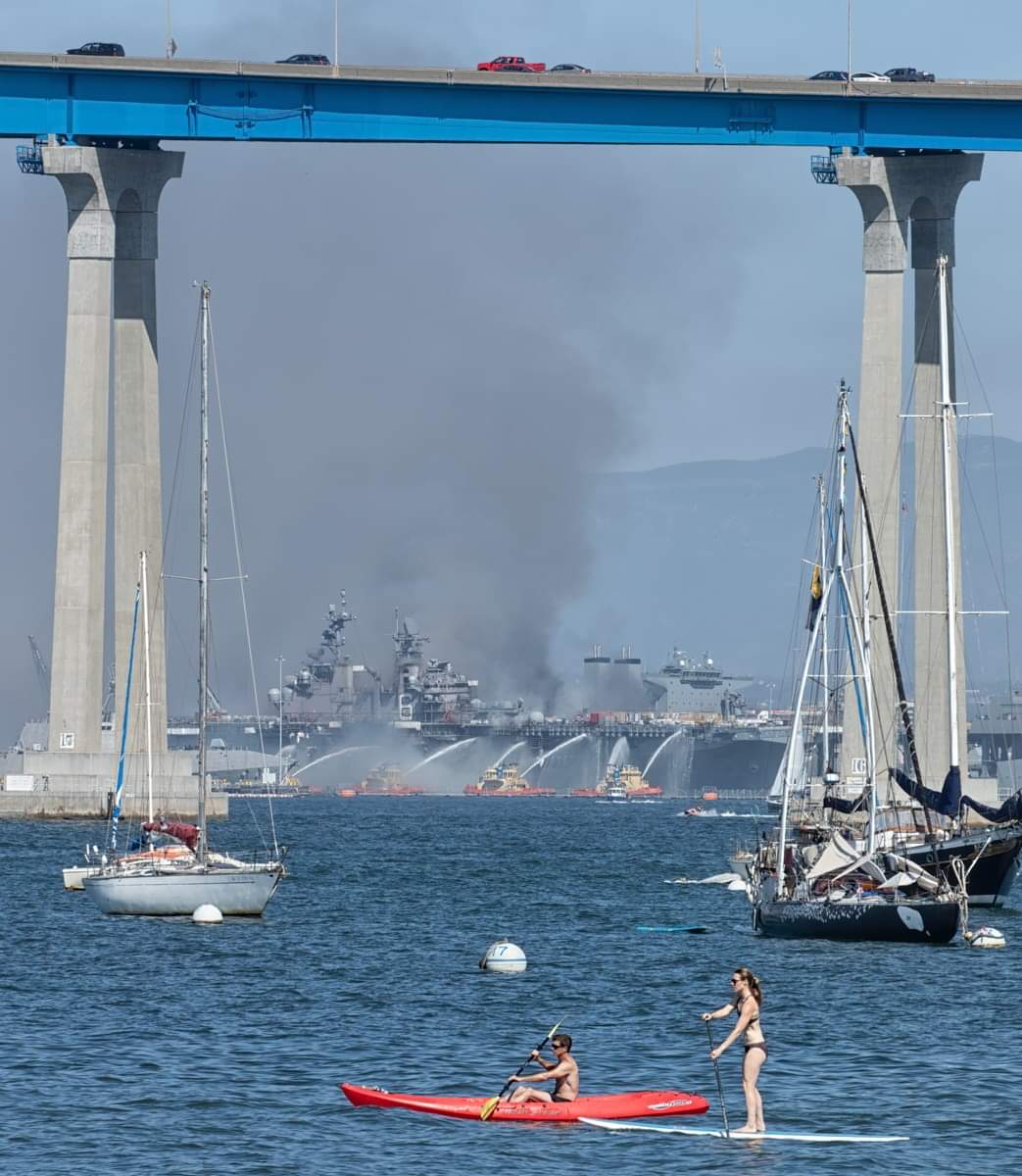 The USS Bonhomme Richard burning in the background as a kayaker and SUP pass by on San Diego Bay. #BonhommeRichard #SanDiego #USNavy #NavalBaseSanDiego #USNavy #Navy #SanDiegoBay #Fire #sdfd #Coronadobridge #SOSanDiego #KUSI #photojournalism