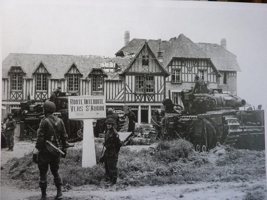 A little later this photo, another well-known one, was taken. It shows Lt Saunders’ AVRE 1D (right) in Bernieres. At the front of the tank is the remains of the log carpet frame. Another AVRE behind the sign will be 1B (from 1408) or 1C (from 1409), both fascine AVREs. 12/12