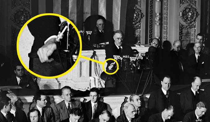 President Franklin Roosevelt gives a speech to congress. His hand is seen gripping the podium upon which several radio microphones sit.