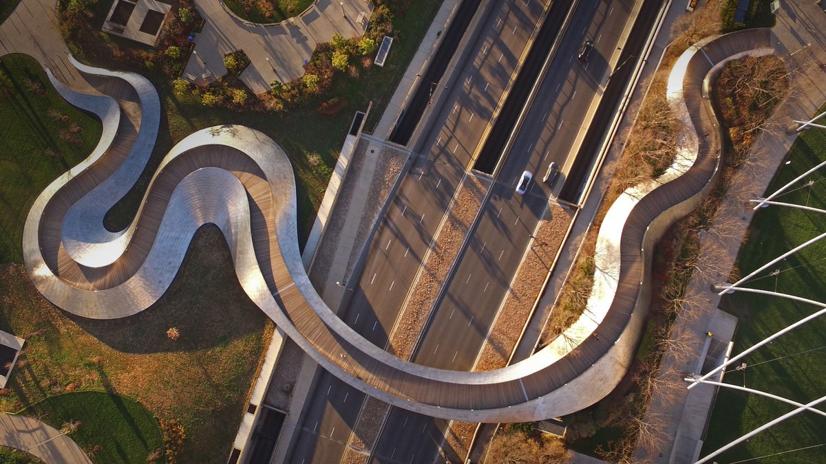 An aerial view of a bridge that winds over a major highway with a snake-like design.