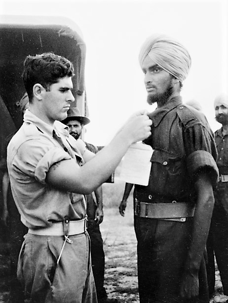 3/9: A man of 5/11 Sikhs, dressed in donated Australian uniform, gets ready to board an ambulance; hospital tag is being pinned by a medic. The Indians were described Australian troops as "very weak but their morale still high” and were "fine men" but "in a desperate state.”