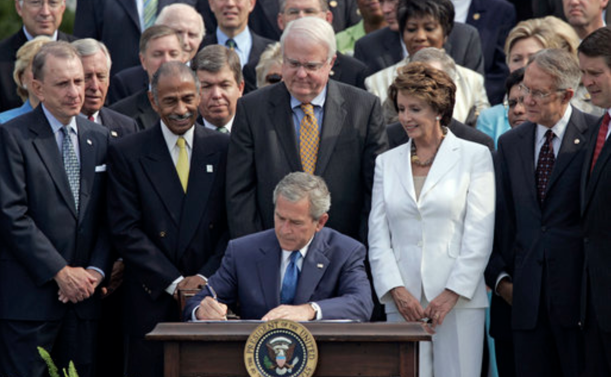 Photo of President George W. Bush signing a reauthorization of the Voting Rights Act in 2006. Lawmakers, including John Conyers, Jim Sensenbrenner, Nancy Pelosi, and Harry Reid, are standing behind him.