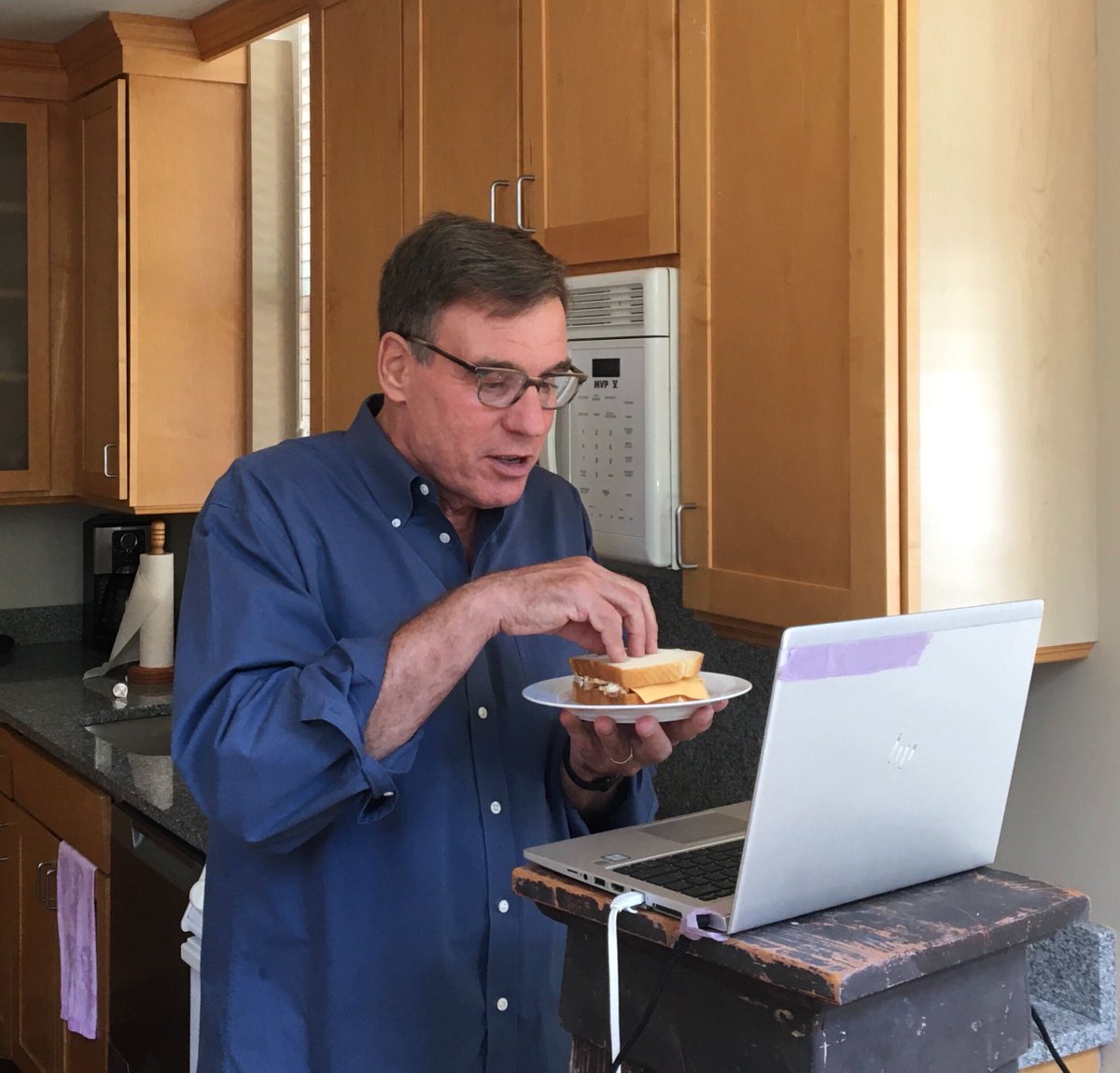 Mark Warner demonstrates his tuna melt as he participates in a Zoom video call.