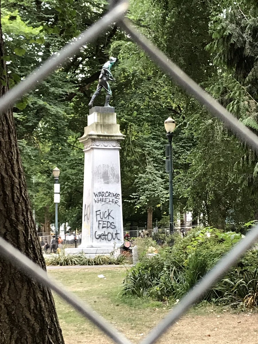 Graffiti on the statue in fenced-off Chapman square refers to Portland’s mayor as “Warcrime Wheeler” and says “Fuck feds get out”
