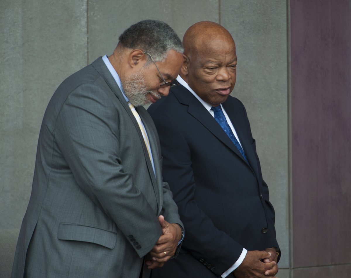 Two men are seen from the side in a color photo. Both wear s