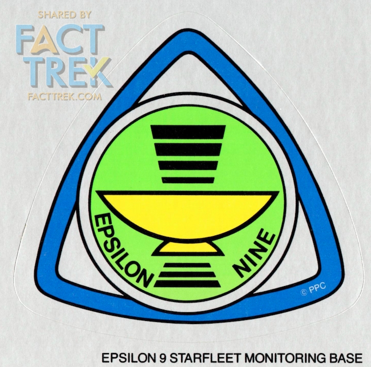 The crew of comm station Epsilon Nine aren’t called out as Starfleet and don’t wear the Flying A. Their emblems represent communications antenna dishes with signals. Signage of that emblem in the Star Trek—The Motion Picture Peel Off Graphics book gives it more detail.