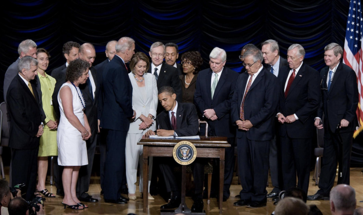 Photo of President Obama signing Dodd-Frank into law, which was 10 years ago today. Lawmakers and Vice President Biden are standing behind him.