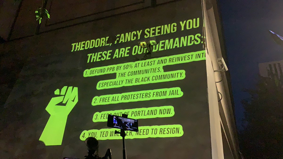 This is being projected above Wheeler: Theodore, fancy seeing you here. These are our demands: defund PPB by 50% at least and reinvest into the communities, especially the Black community Free all protesters from jailFeds out of Portland nowYou Ted Wheeler need to resign