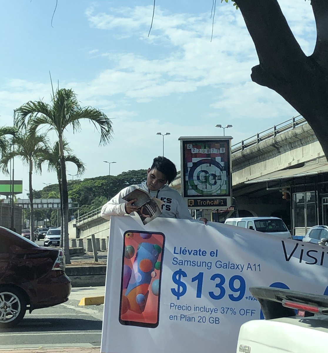 mariasolponsc's tweet photo. Este chico #trabaja sosteniendo un cartel de una telefónica mientras #lee un libro a las 3pm bajo el sol de #Guayaquil. Este chico me da esperanza. #lacallehabla #leertehacelibre #writerslife https://t.co/EybrqR9ZLN