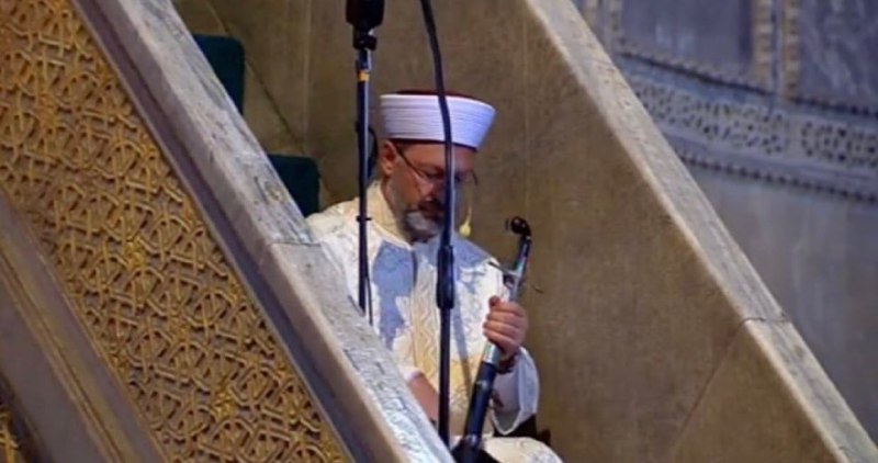 Osmanlı‘da fethedilen yerlerdeki en büyük kilise camiye çevrilirken fethin sembolü olarak caminin minberine iki sancak asılır ve minberin sağ giriş tarafına bir kılıç koyulurdu. İşte o kılıç ve sancaklar yeniden konuldu. İmamımız Ali Erbaş hutbeyi kılıçla okuyor. #AyasofyaCamii
