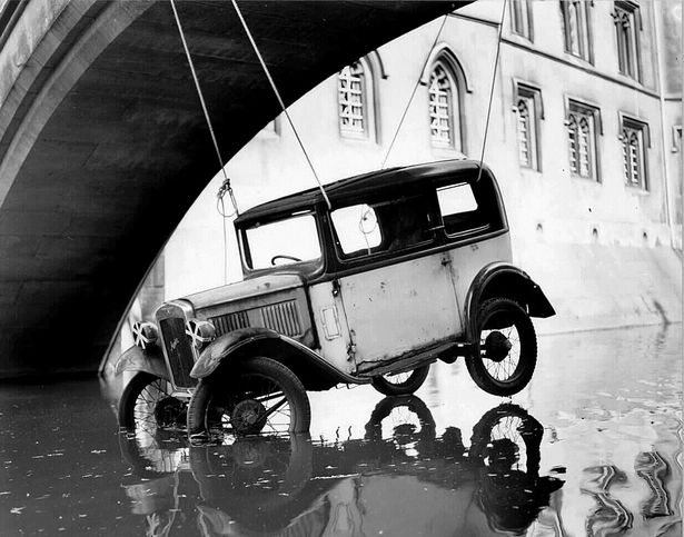 The car was by punted along the river and when under the bridge, they passed cables through the open windows of the car, then through the windows of the bridge, and tightened them up. Thanks Julian Fowler for revealing all ;)