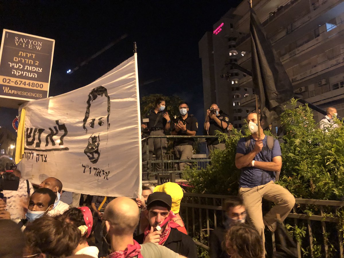 The faces of Eyad al-Hallaq and Solomon Teka, both victims of police violence, are being held aloft in front of a group of police filming the protestors