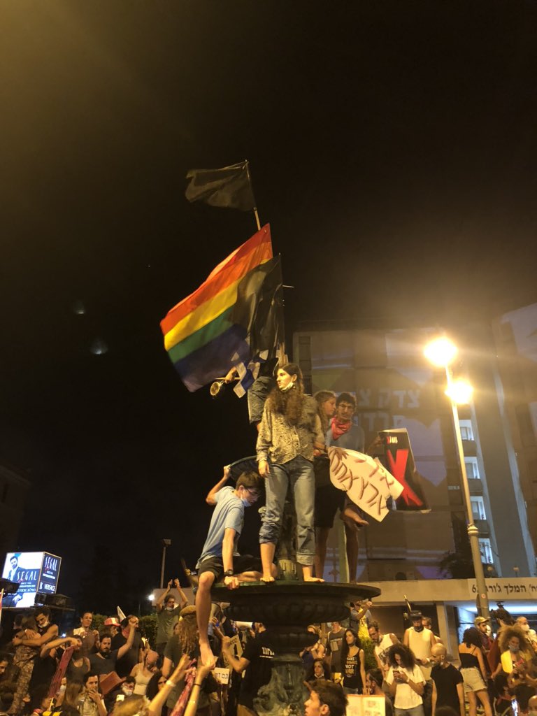 A pride flag flies next to an Israeli flag and several black flags above the fountain in the centre of the square. Meanwhile, the water in the fountain had been dyed red