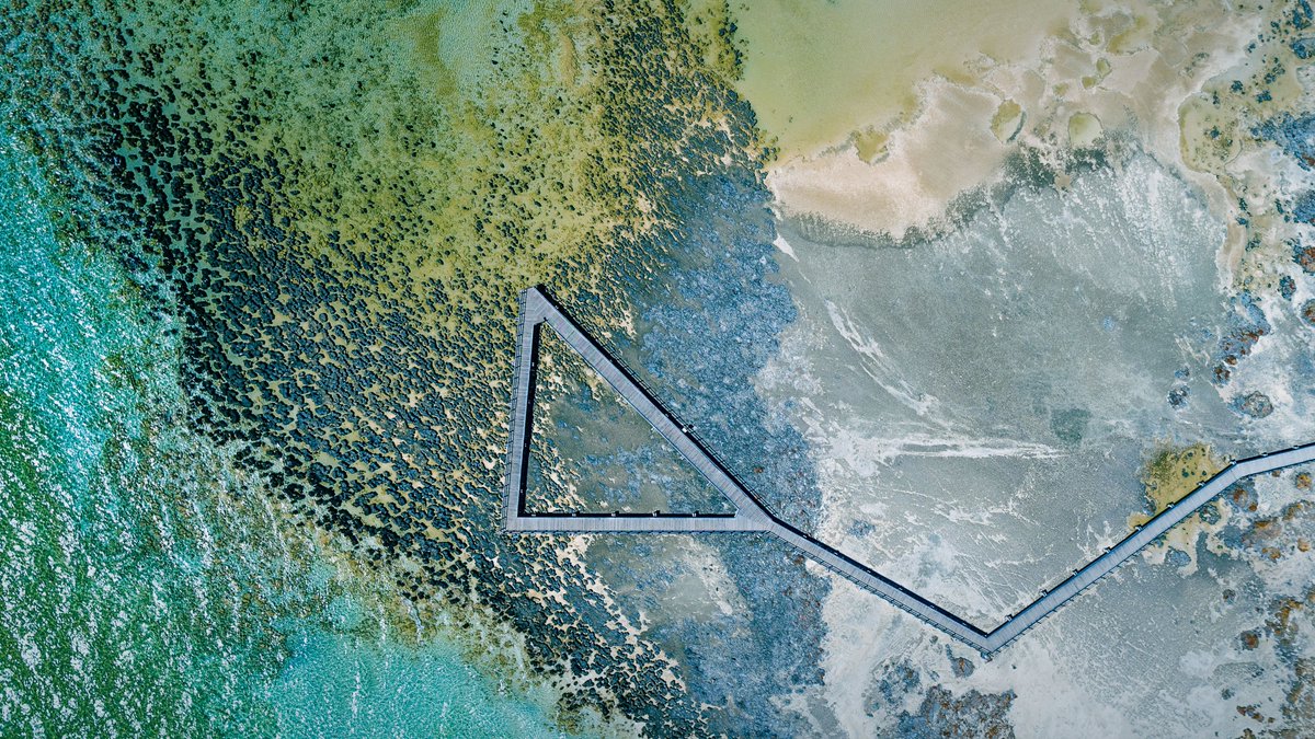 A boardwalk extending into aquamarine water forming a triangle when viewed from above.