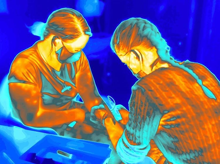 geshNHS's tweet photo. "We find ourselves living in an age when body temperature has assumed a new set of implications." - @GilesInfo has used a thermal camera to capture a new set of images for @NatGeo. This one shows a participant in a Covid-19 vaccine trial having her blood taken at St George's. 📸 https://t.co/VZHrwBenoA