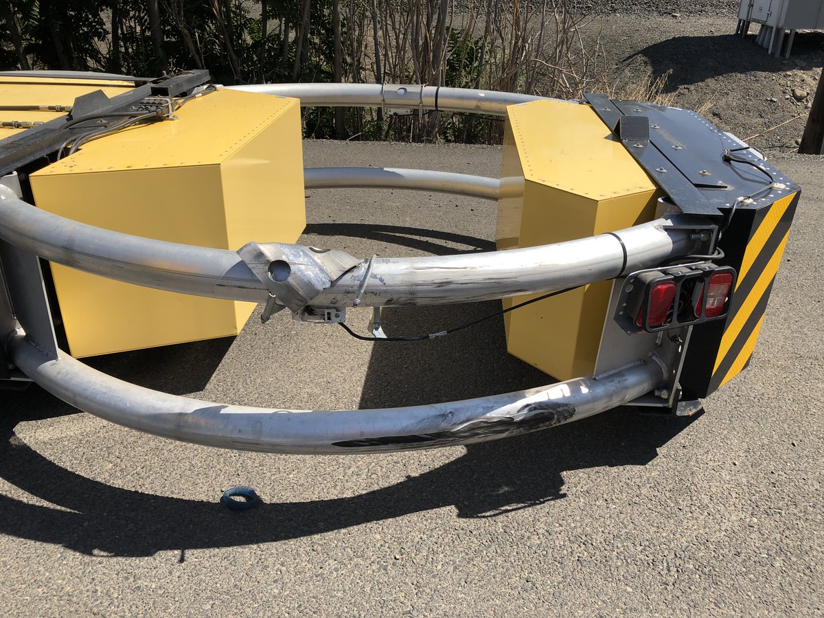 The back end of a construction vehicle with some damage to it after it was struck by another vehicle.