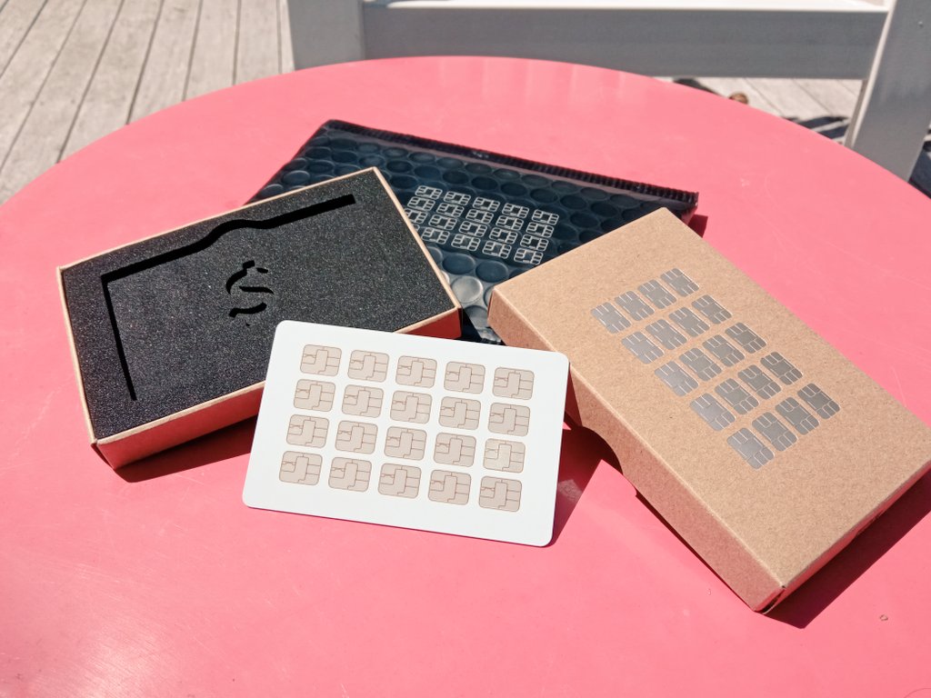 a white debit card, with a 4 by 5 row grid of chips on the front. behind it is packaging and a red table.