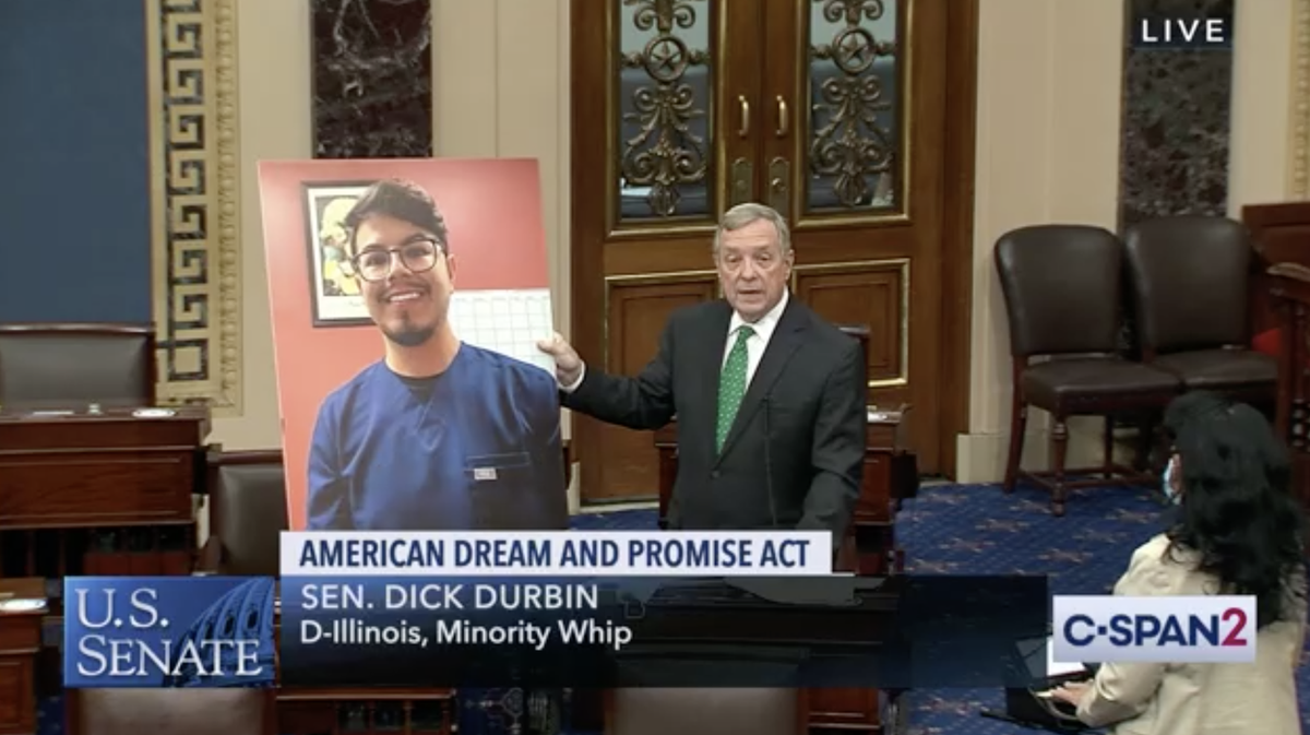 Screenshot of Senator Durbin speaking on the Senate floor and holding up a poster showing the image of a Dreamer.